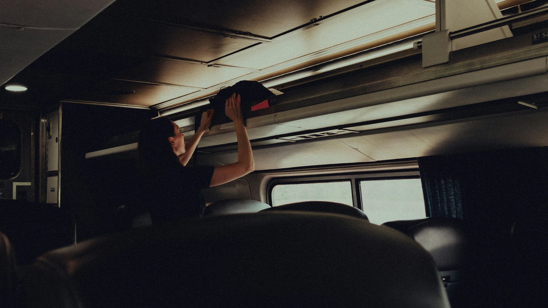 A woman placing her bag in the overhead rack on a modern train.