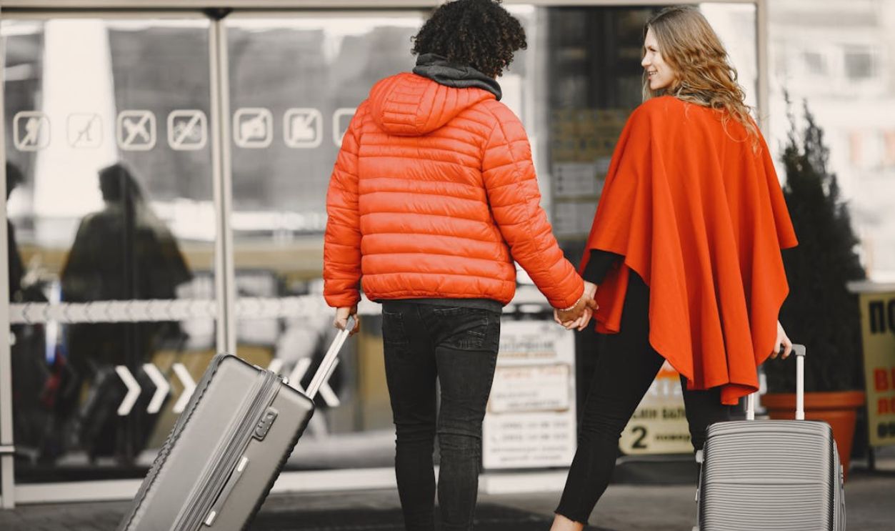 A couple holding hands with luggage, entering an airport for a travel journey.