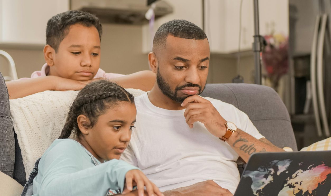 A father and his two children engaged together while using a laptop at home