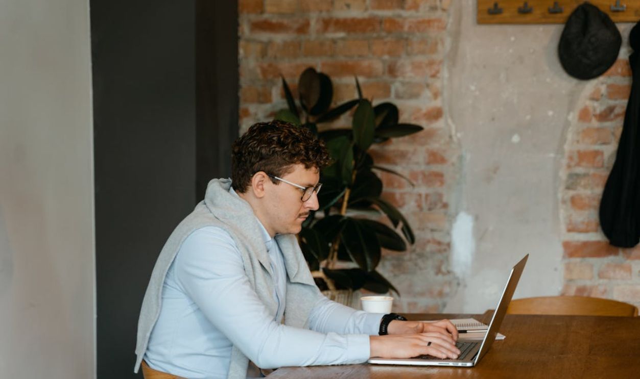 Man typing on laptop at a wooden desk in a cozy, rustic office space