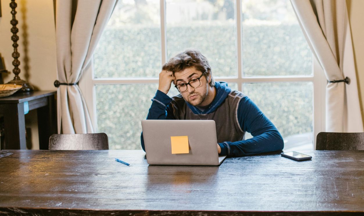 Man in casual attire working on a laptop at a wooden table in a cozy room