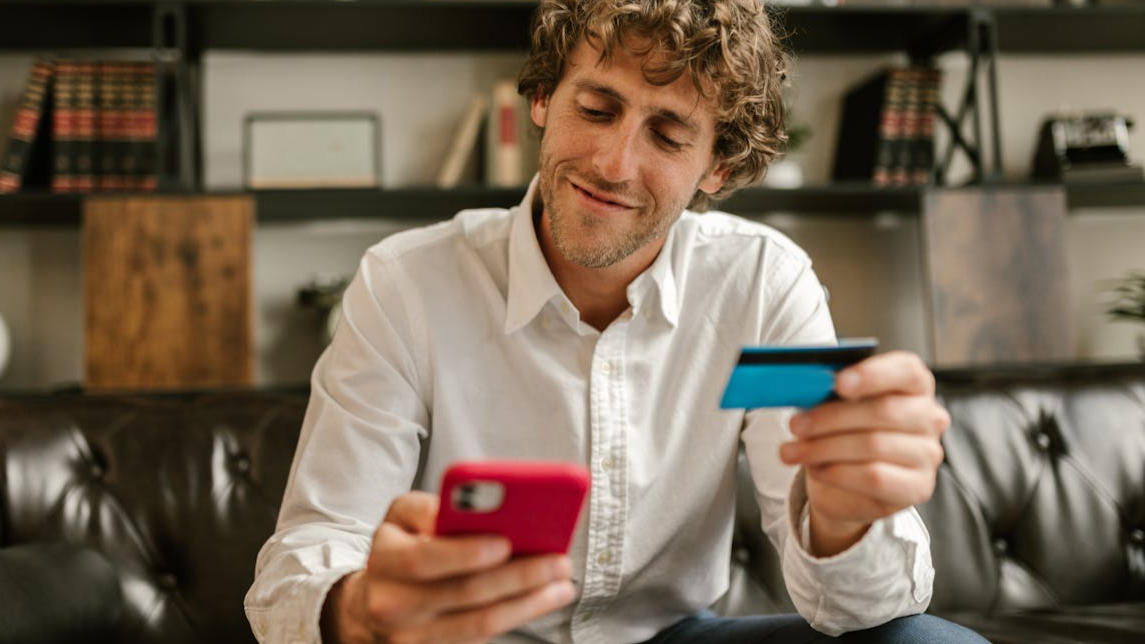 Caucasian man using smartphone and credit card for online shopping indoors