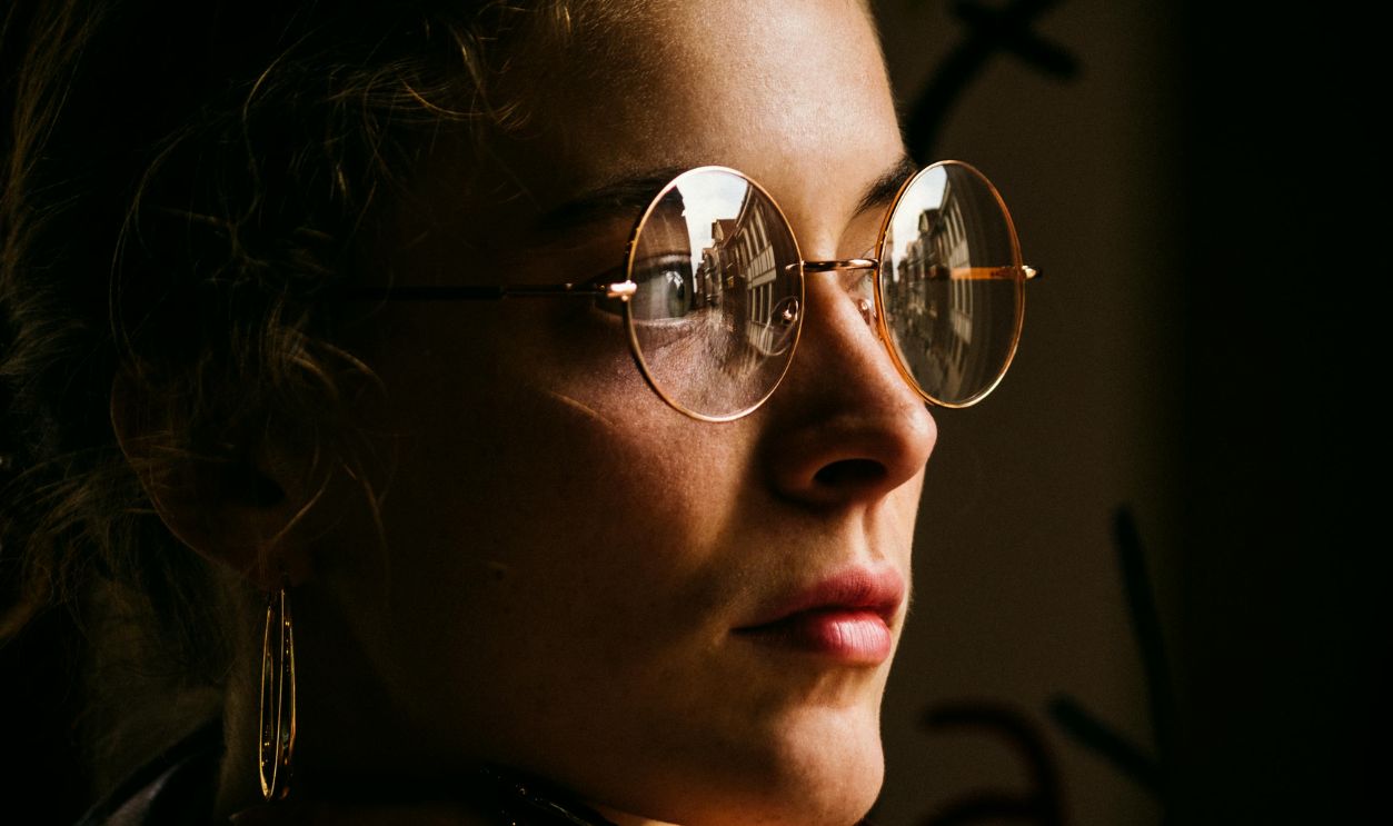 A woman gazes thoughtfully, cityscape reflected in her sunglasses, enhancing introspection