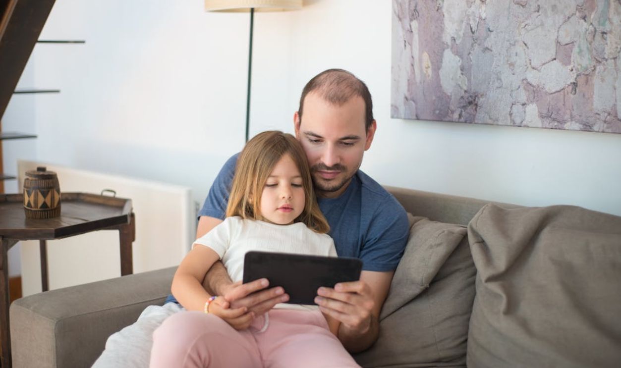 A father and daughter enjoying quality bonding time together on a couch using a tablet