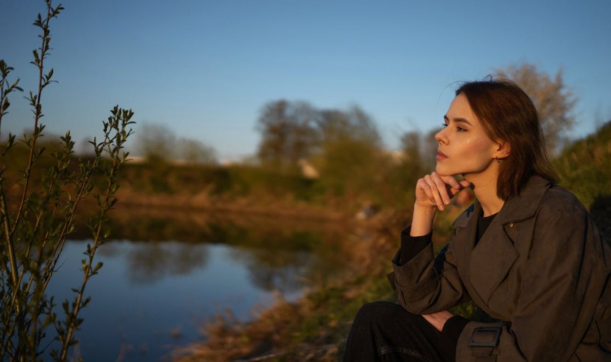 A woman sitting by a lakeside, contemplating nature during sunset