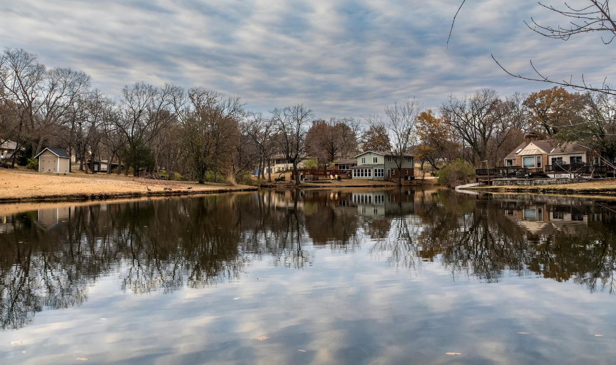 Peaceful autumn scene of lakeside homes reflecting on tranquil water in Platte Woods
