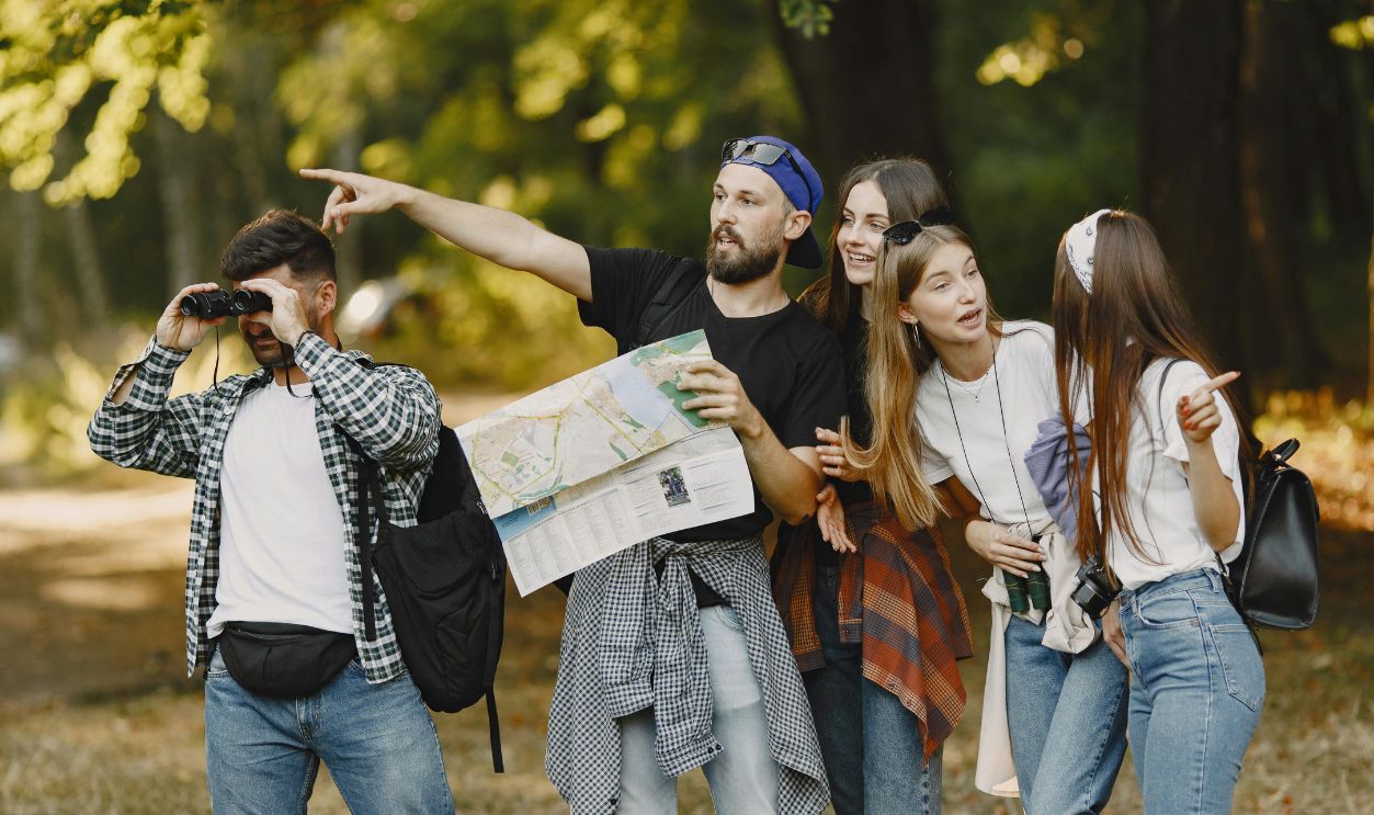 Group of friends navigating nature with map and binoculars, enjoying a summer hike