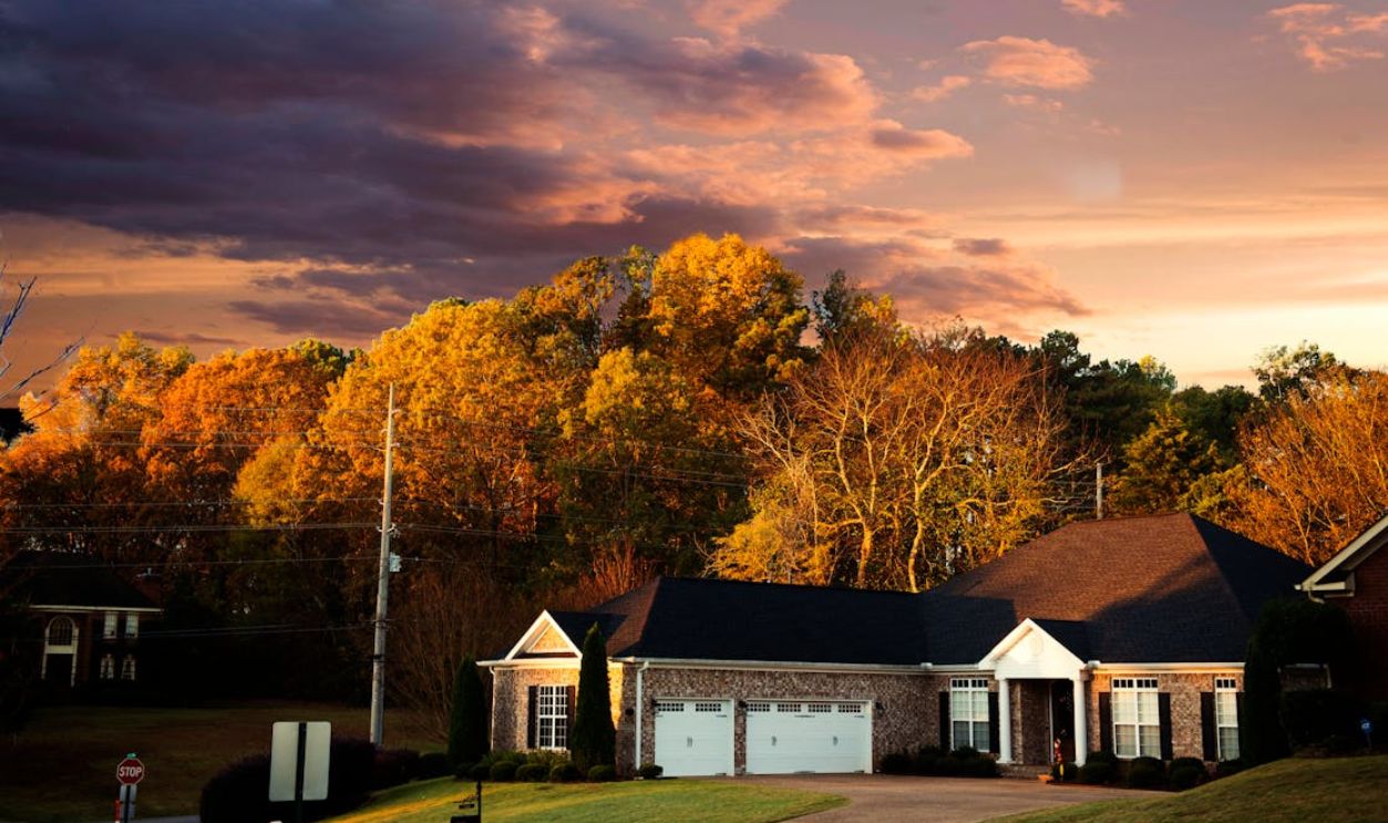 A picturesque suburban house surrounded by fall foliage under a dramatic sunset sky in Madison, AL