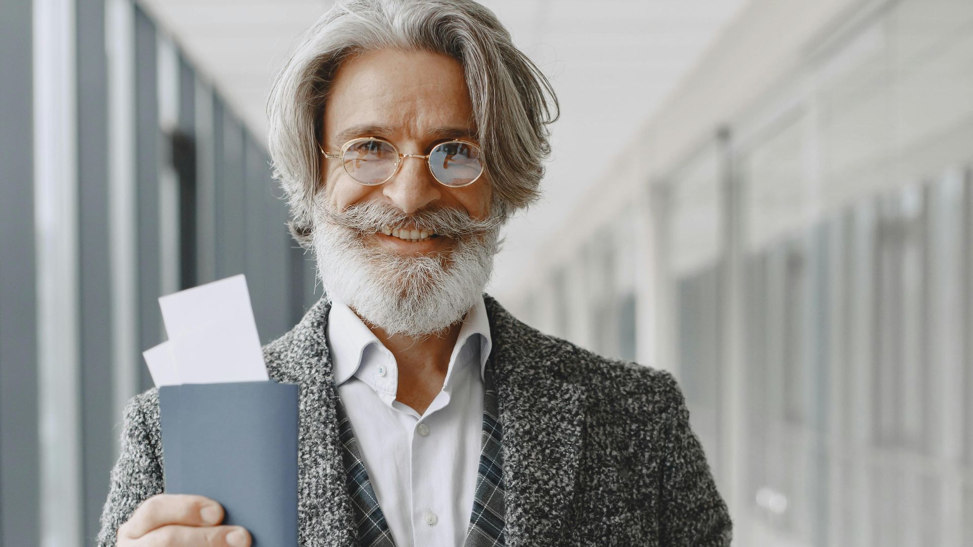Elderly man in airport holding passport and luggage, smiling confidently at the camera.