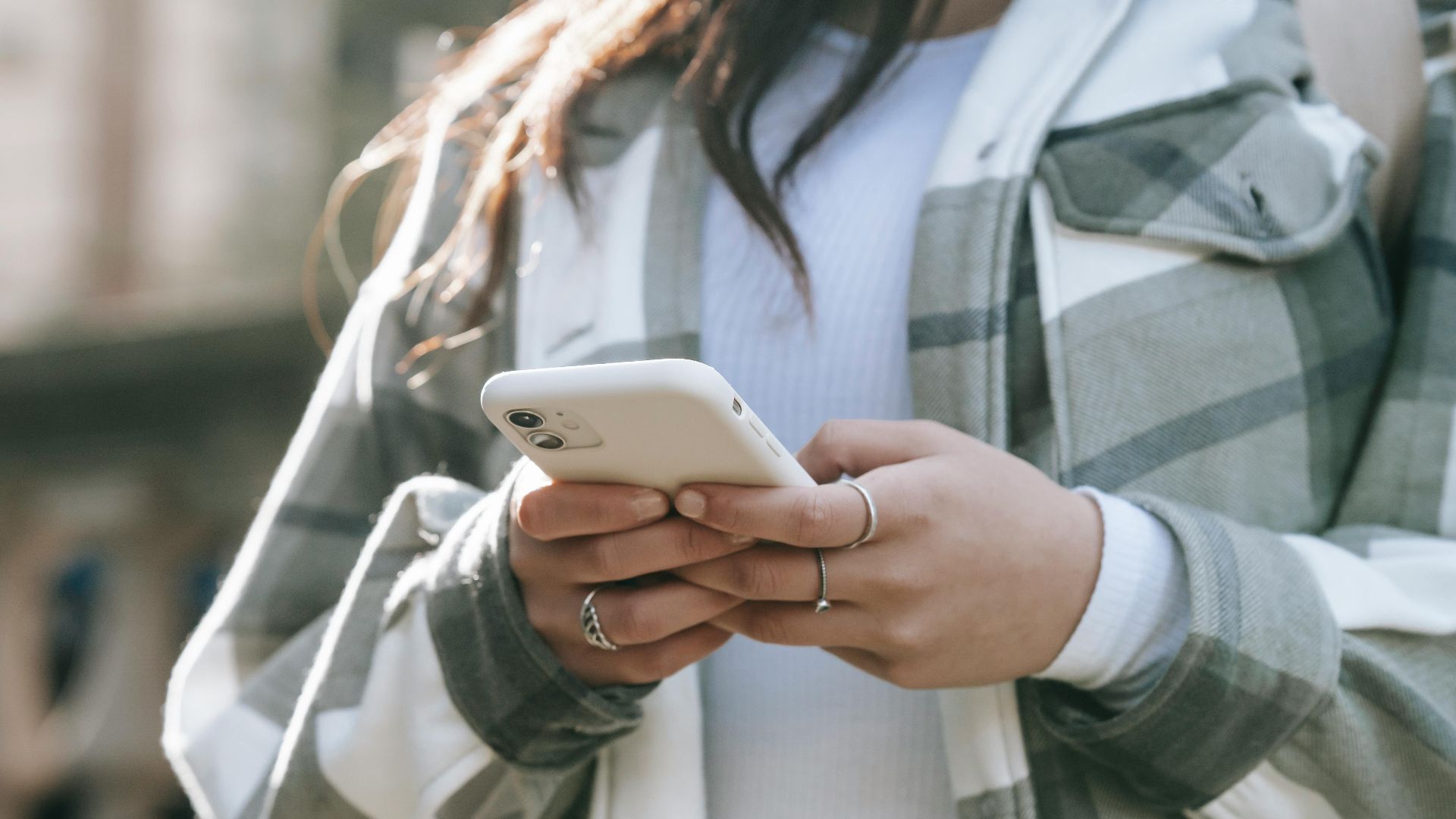 Crop faceless young woman in casual outfit text messaging on phone in city street in daytime