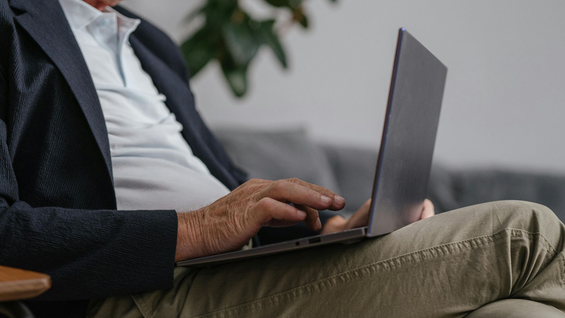 Close-up of a man in a suit jacket using a laptop indoors, showcasing a relaxed work environment.