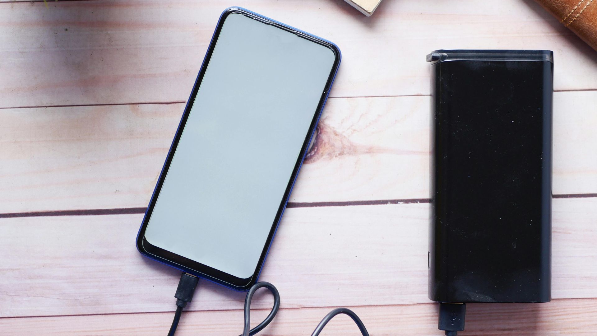 Smartphone charging with a power bank on a wooden desk, showcasing modern technology essentials.