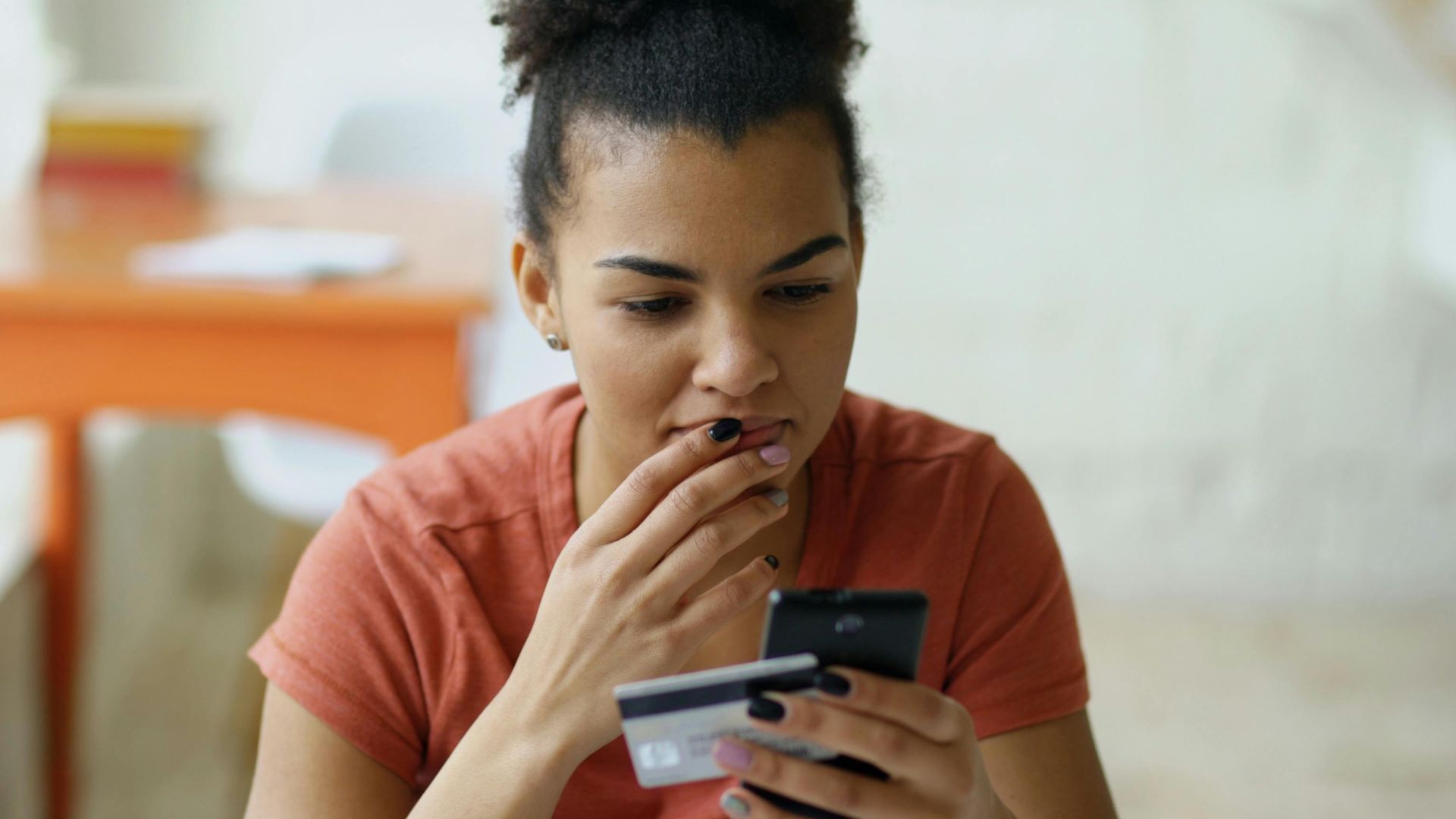 Young woman shopping online using a smartphone and credit card indoors.