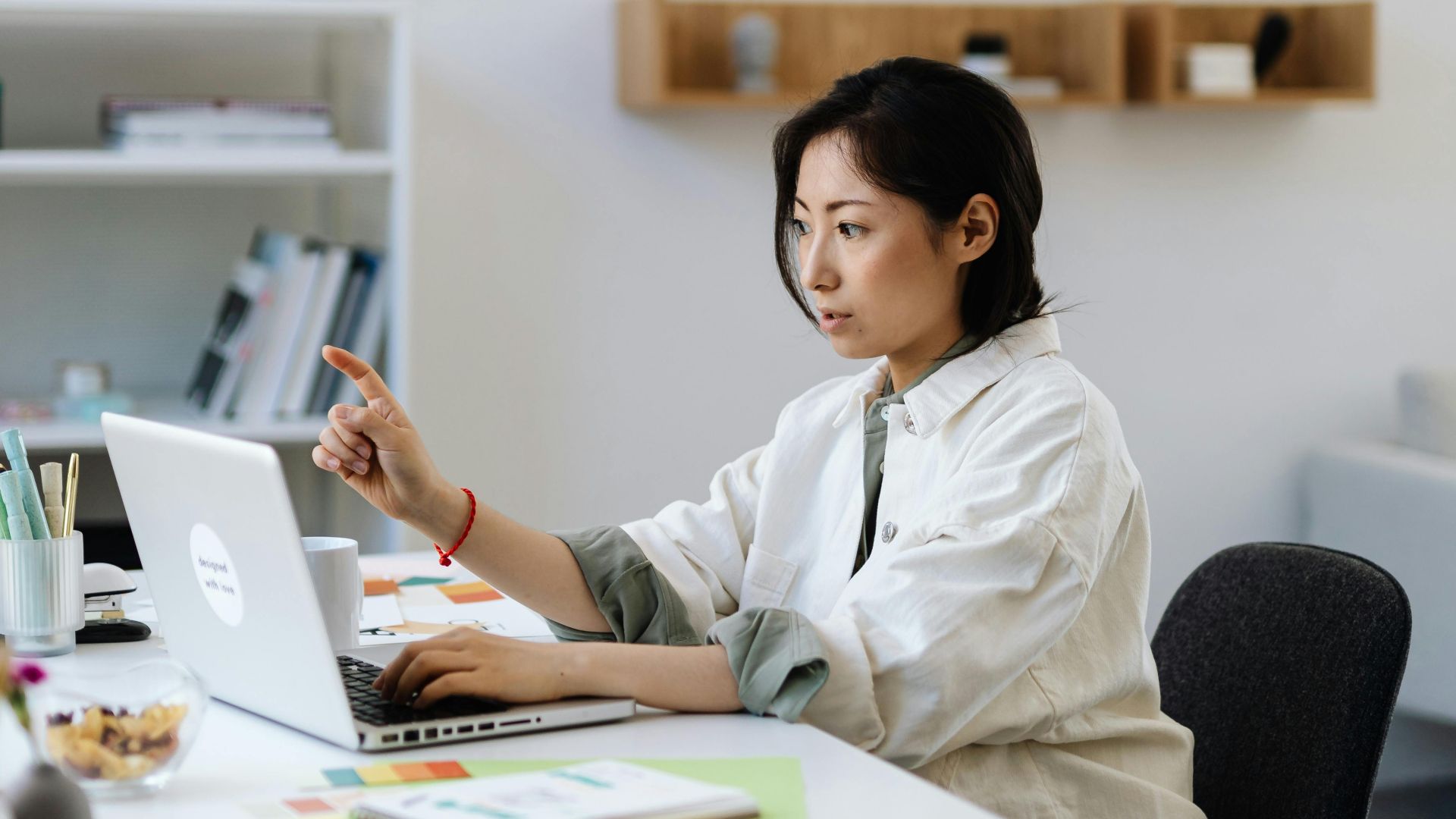 Professional Asian woman focused on laptop work in a modern and minimalistic office setting.