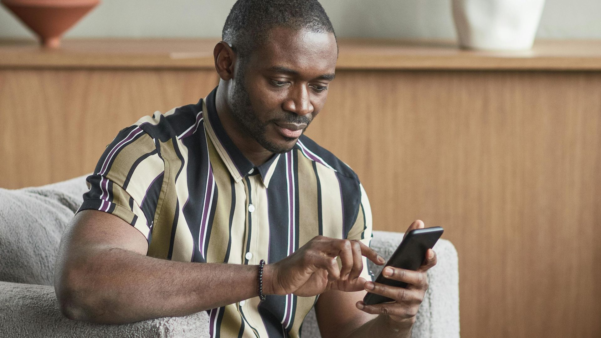 Casually dressed man sitting in armchair using smartphone in modern living room.