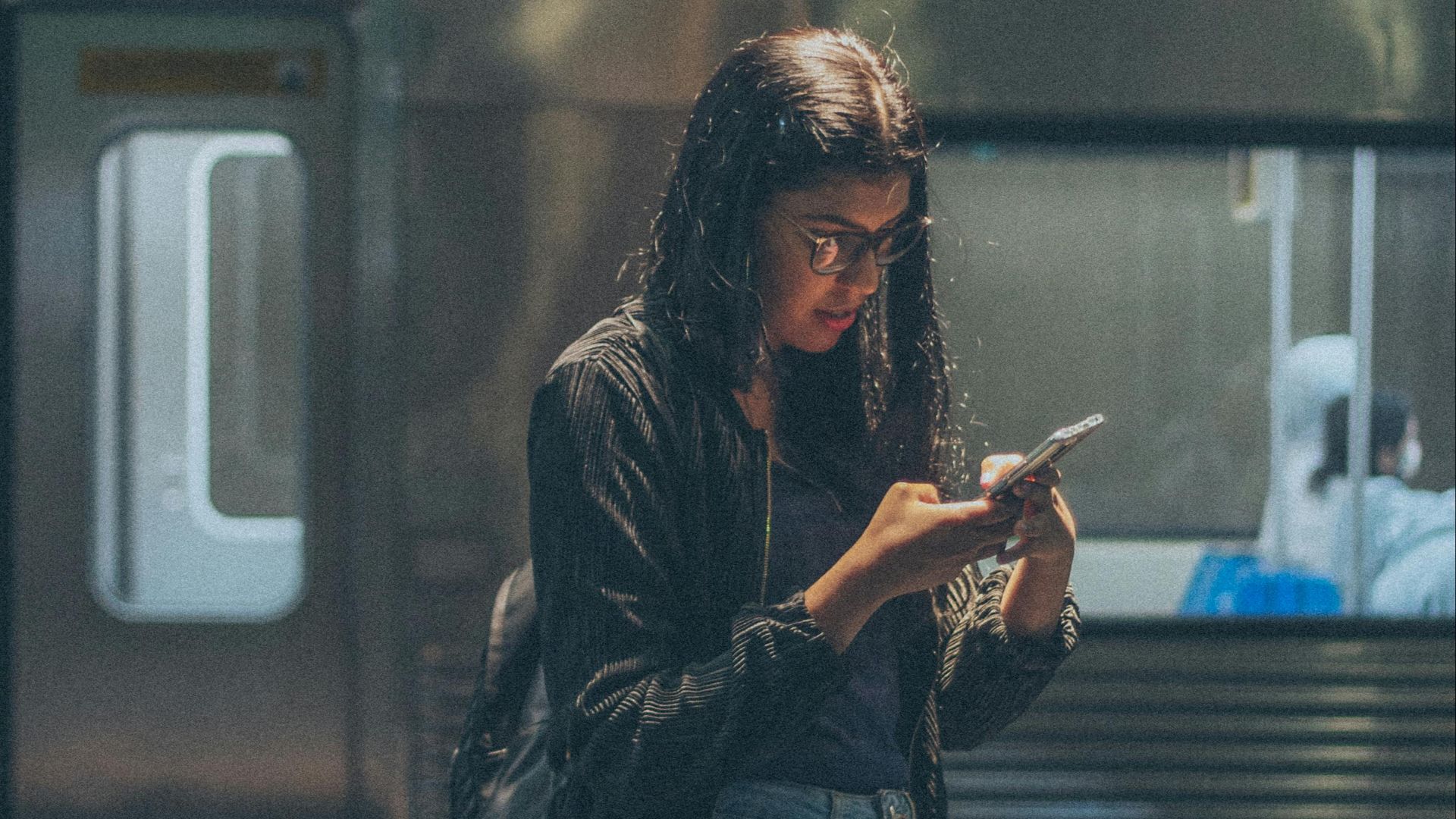 Young woman in denim pants using a smartphone at urban train station. Casual style and modern lifestyle.