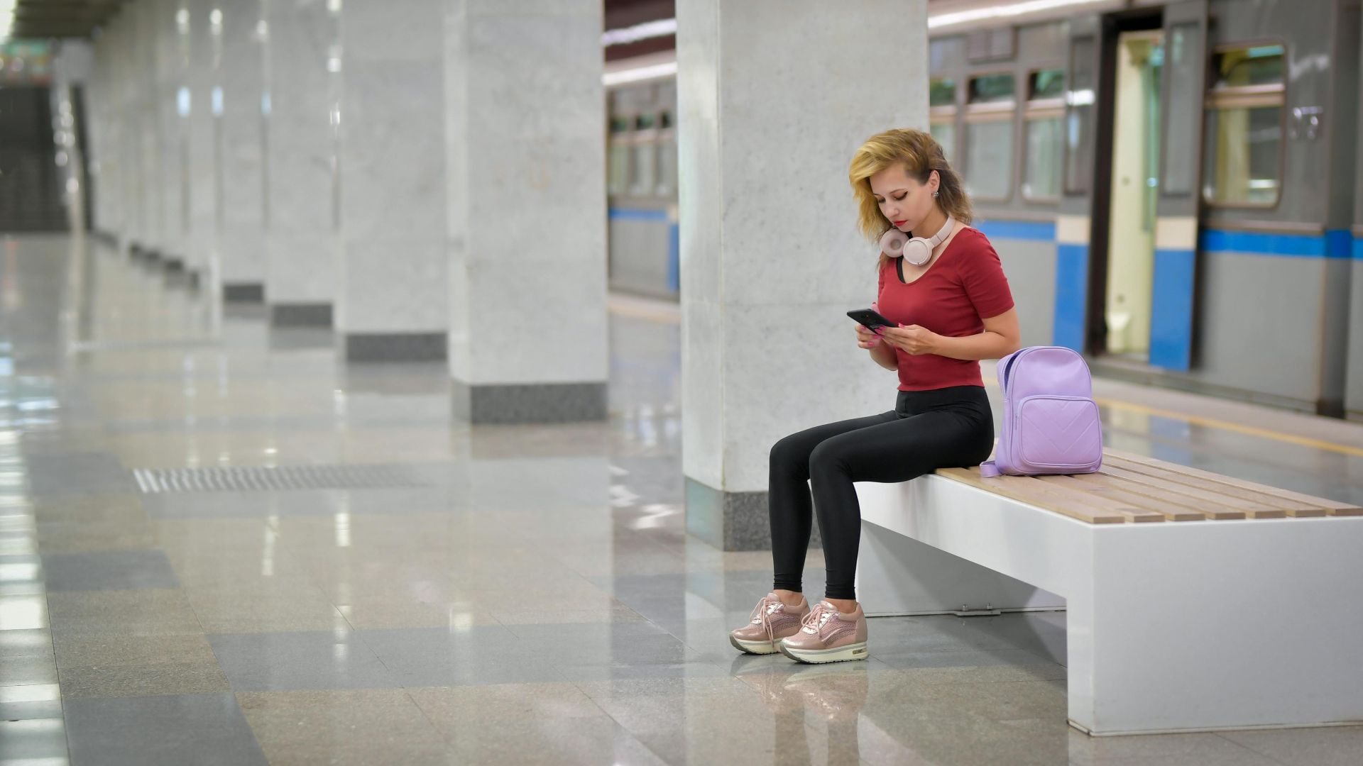 Young woman in a subway station checking her smartphone while waiting for a train.