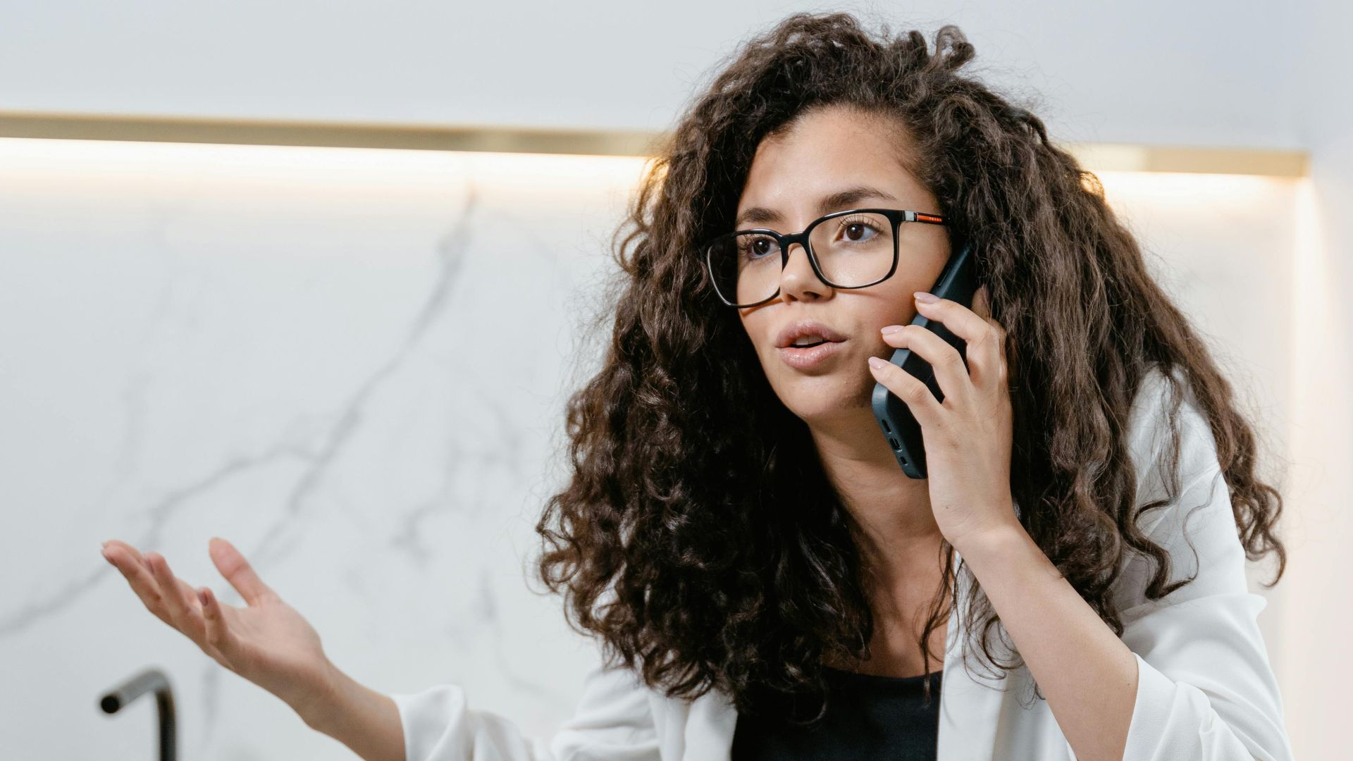 An adult woman discussing on the phone in a stylish modern kitchen setting.