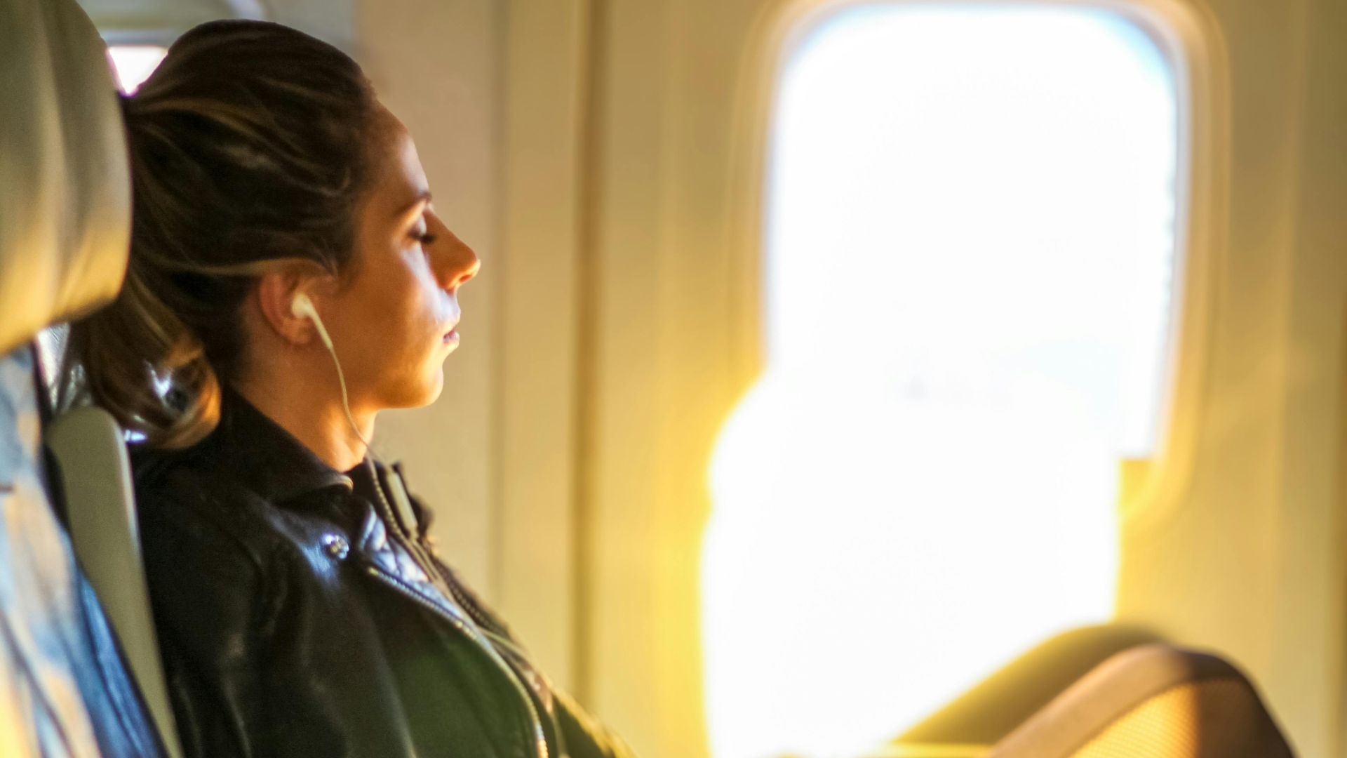 A woman enjoys a tranquil moment on a flight, gazing out the window with headphones on.