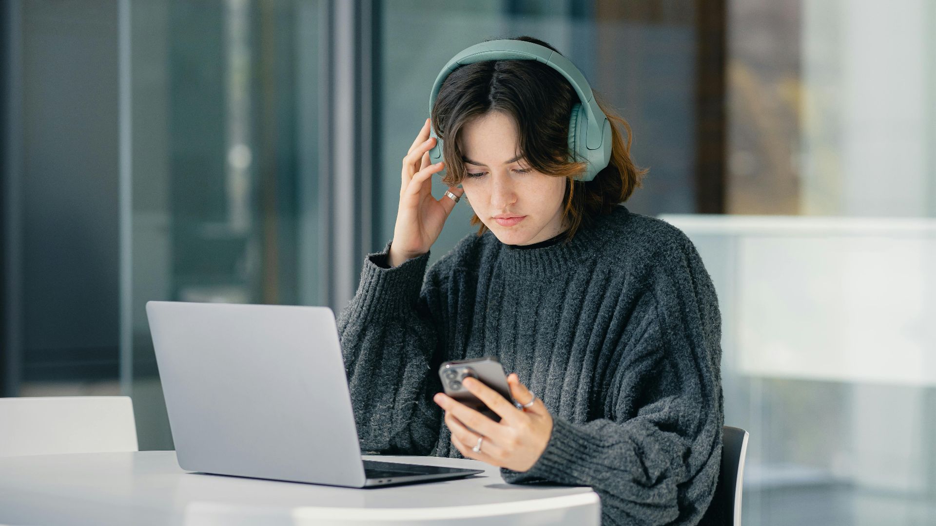 Focused young woman with headphones using laptop and smartphone in a modern cafe.
