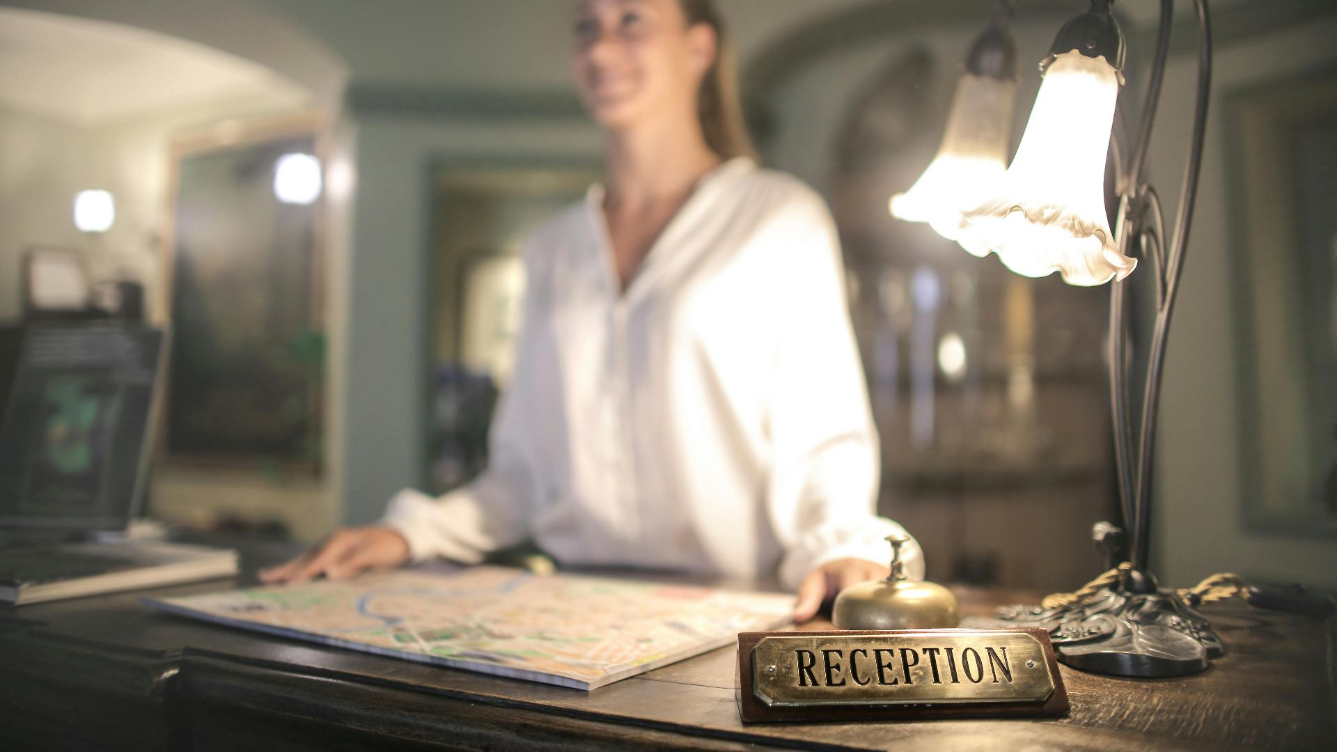 Blurred female in white shirt standing at reception desk with map on table and smiling while looking away
