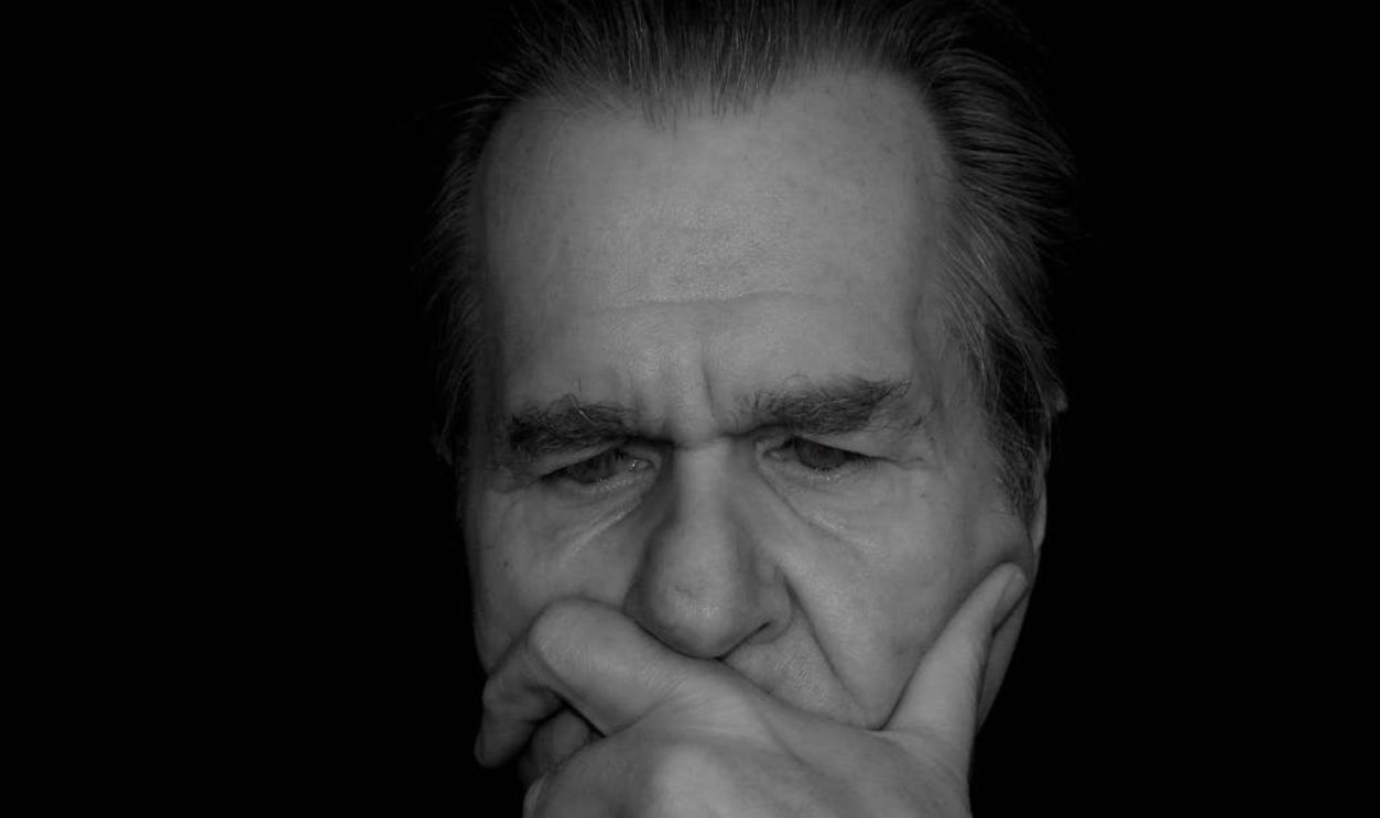 Close-up portrait of a thoughtful elderly man against a dark background