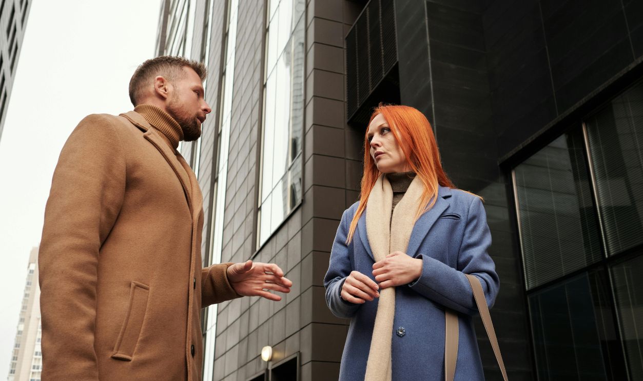 Two adults engage in a conversation outdoors between modern city buildings