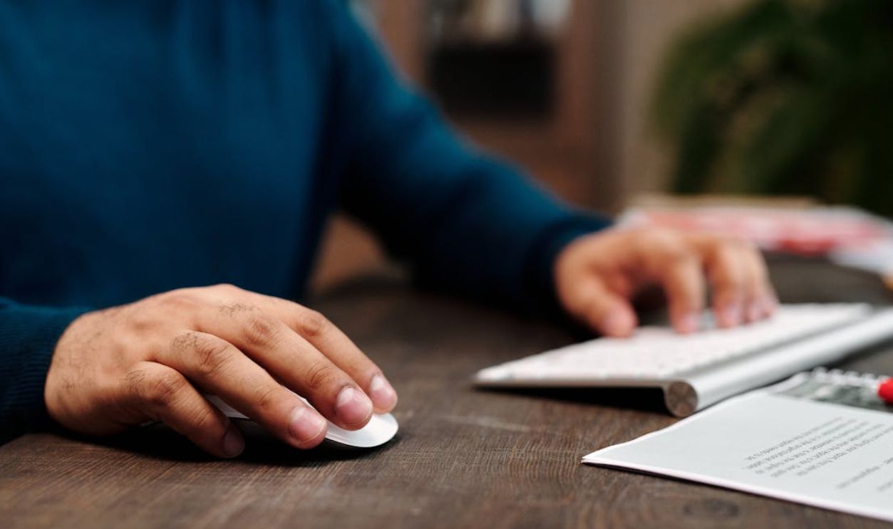 Close-up of a man using a wireless mouse and keyboard on a wooden desk
