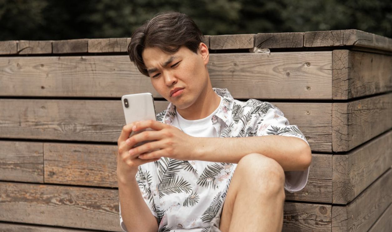 A young man intensely focused on his smartphone while sitting outside on a wooden bench