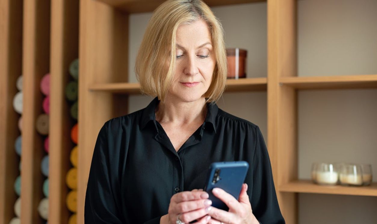Professional woman in black attire using a smartphone indoors with shelving background