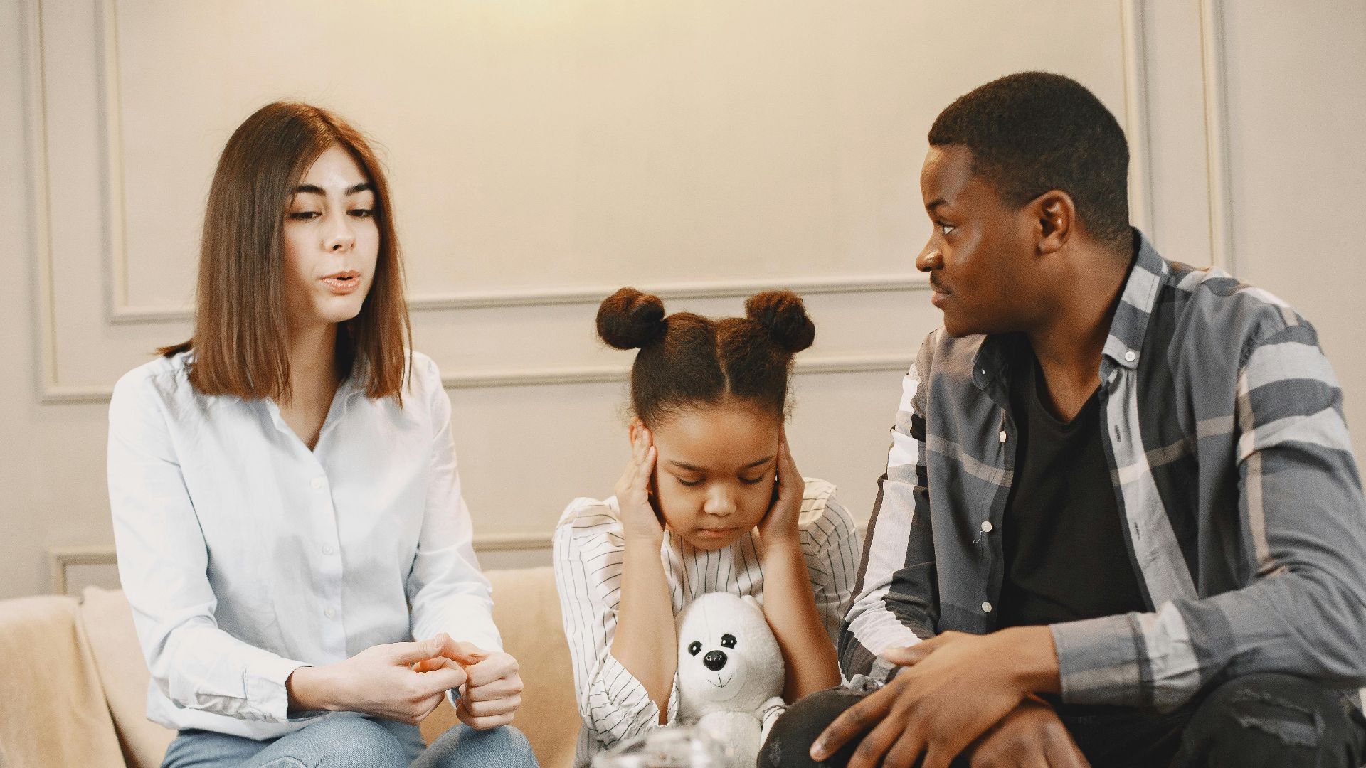 Parents talking to daughter covering ears on sofa.
