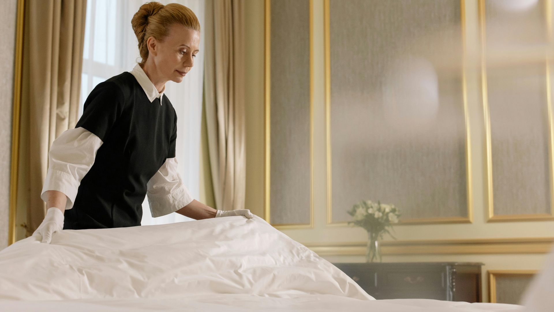A professional housekeeper fixes a bed in a luxurious hotel room.