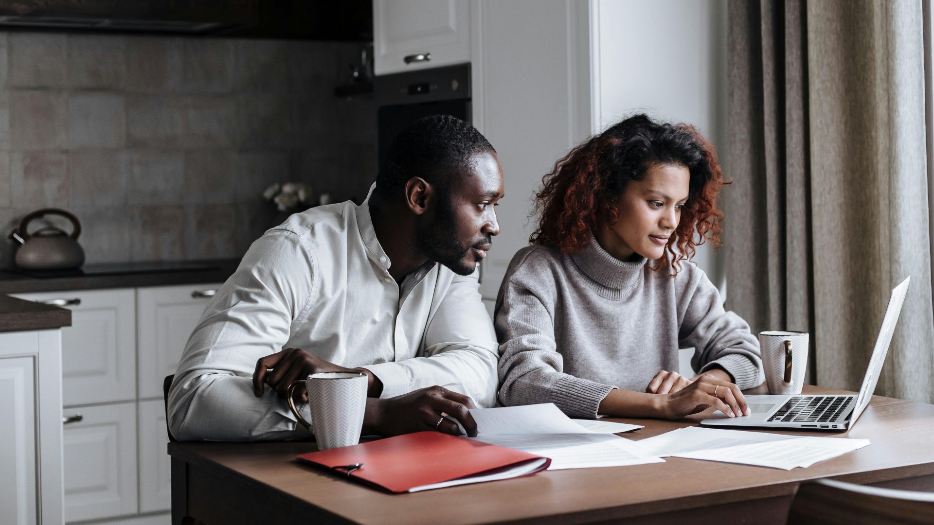 A diverse couple working together on a laptop in a modern kitchen setting, displaying teamwork and collaboration.