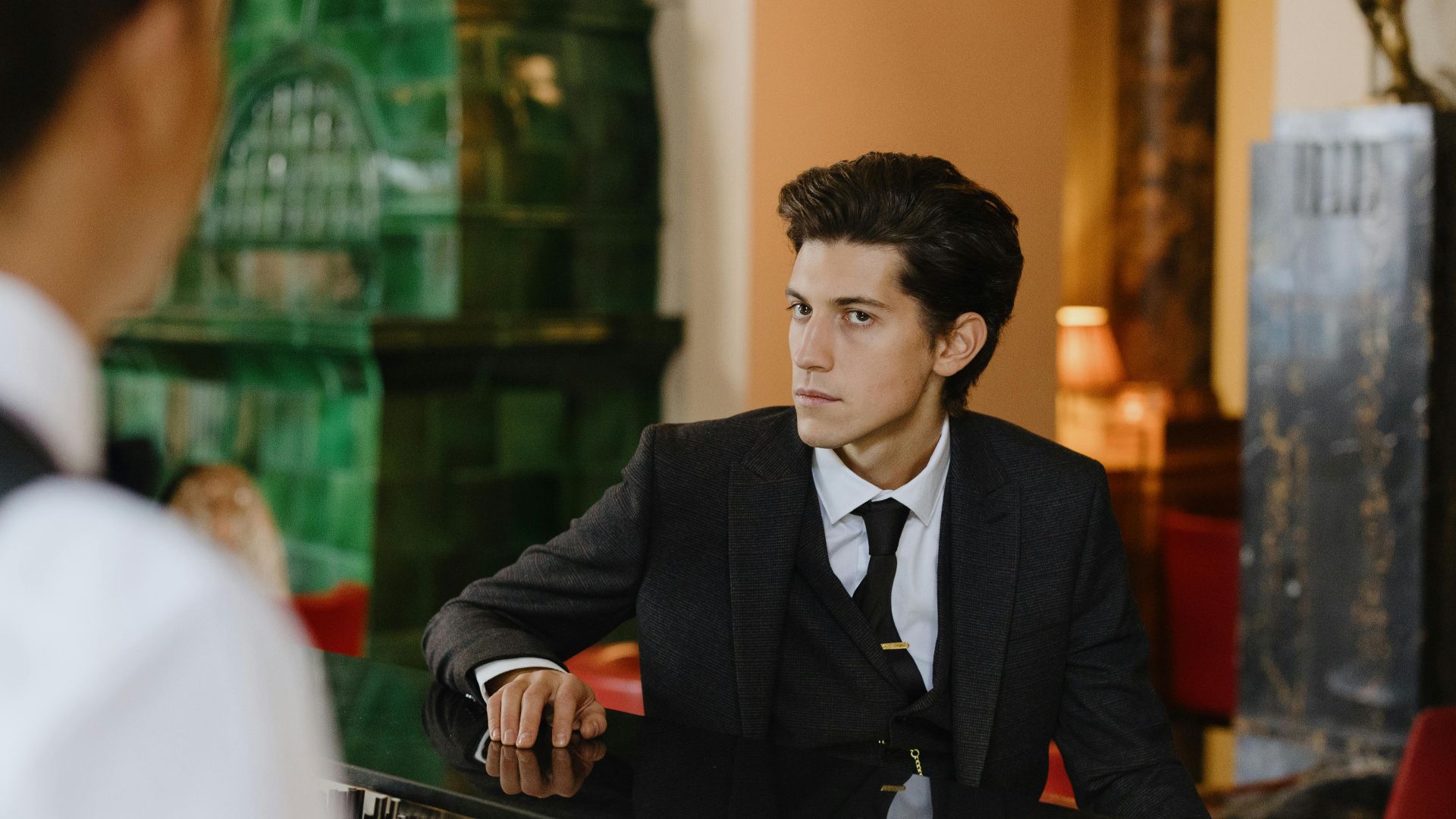 Sophisticated man in a suit sitting at a vintage bar counter indoors, exuding elegance and style.