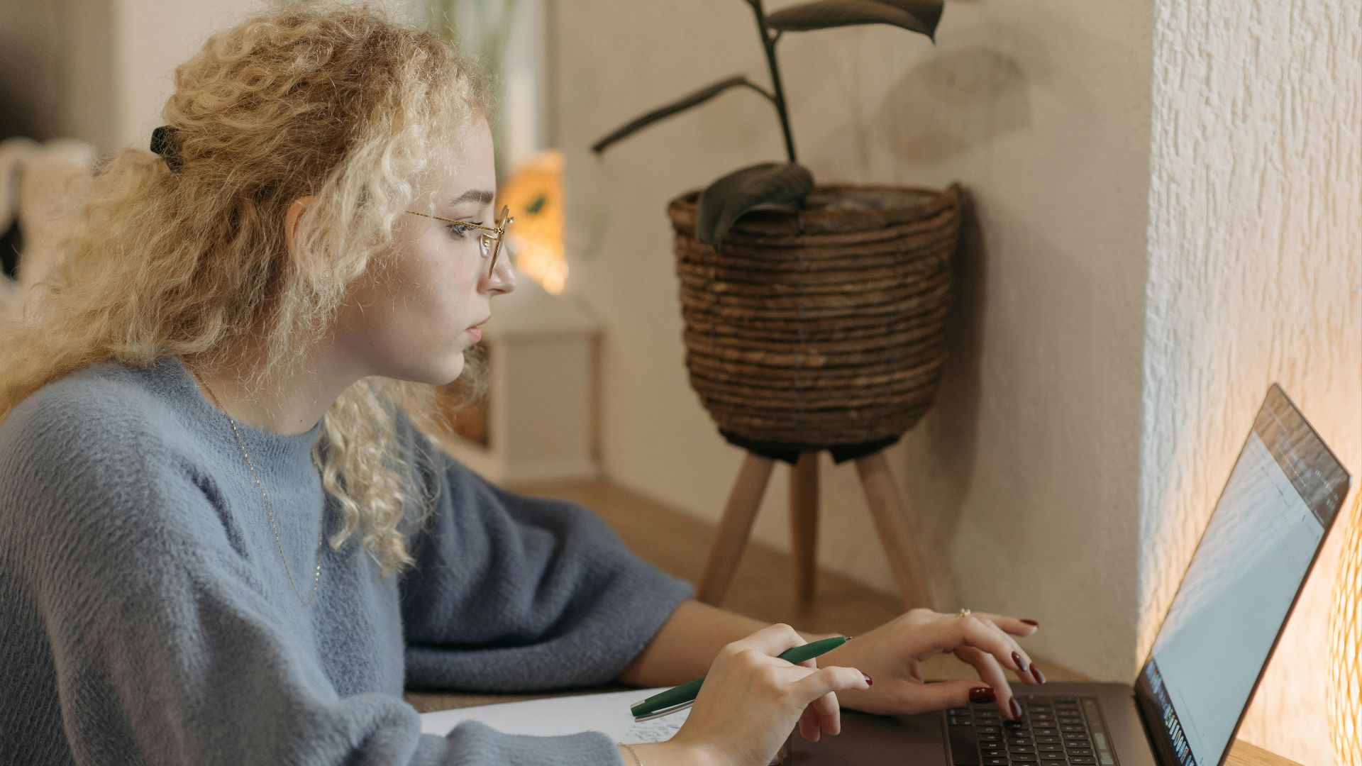 Young woman focused on remote work in a cozy indoor setting with a laptop and coffee cup.