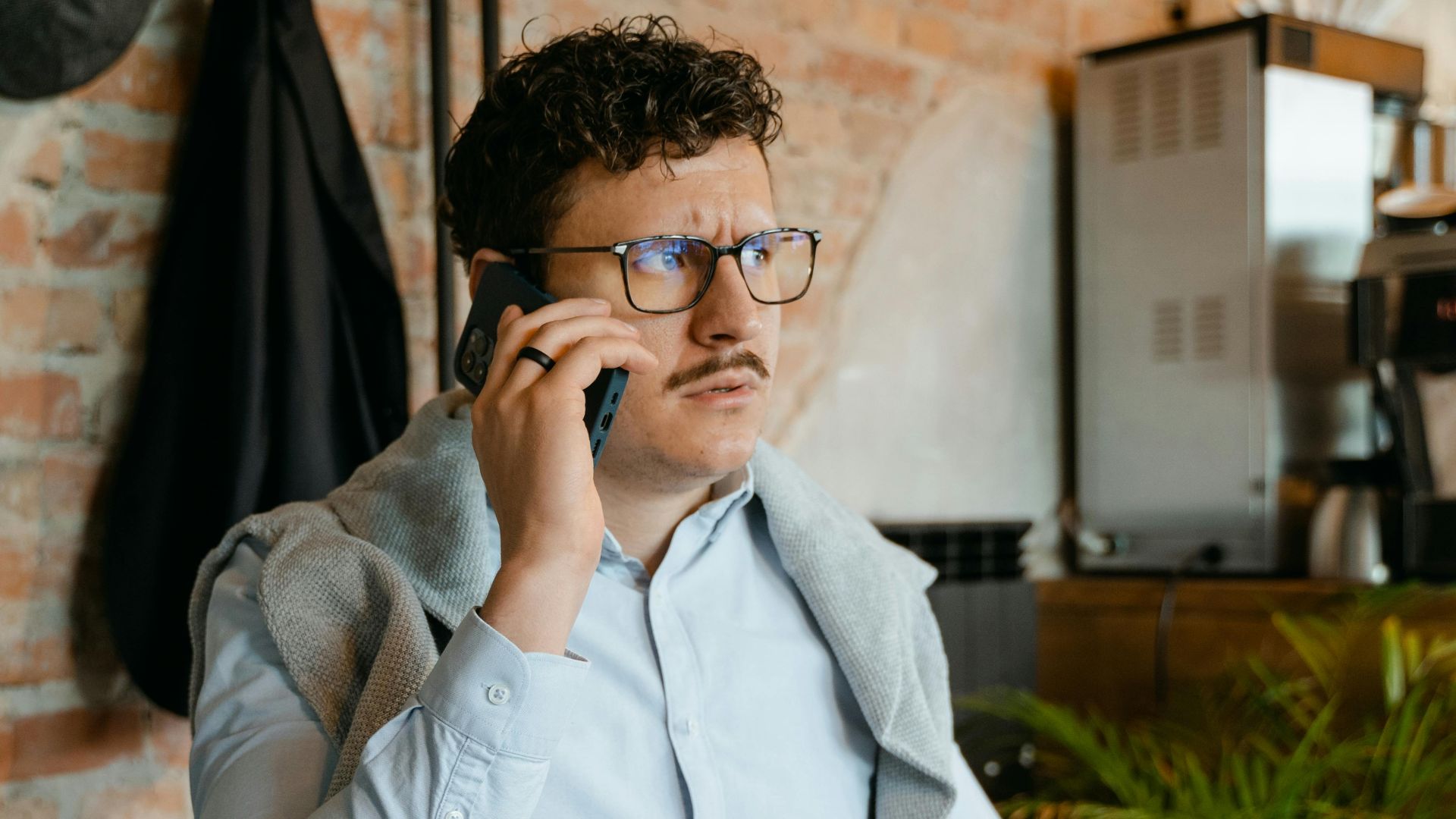 Man with glasses and mustache on a phone call in a cozy cafe.