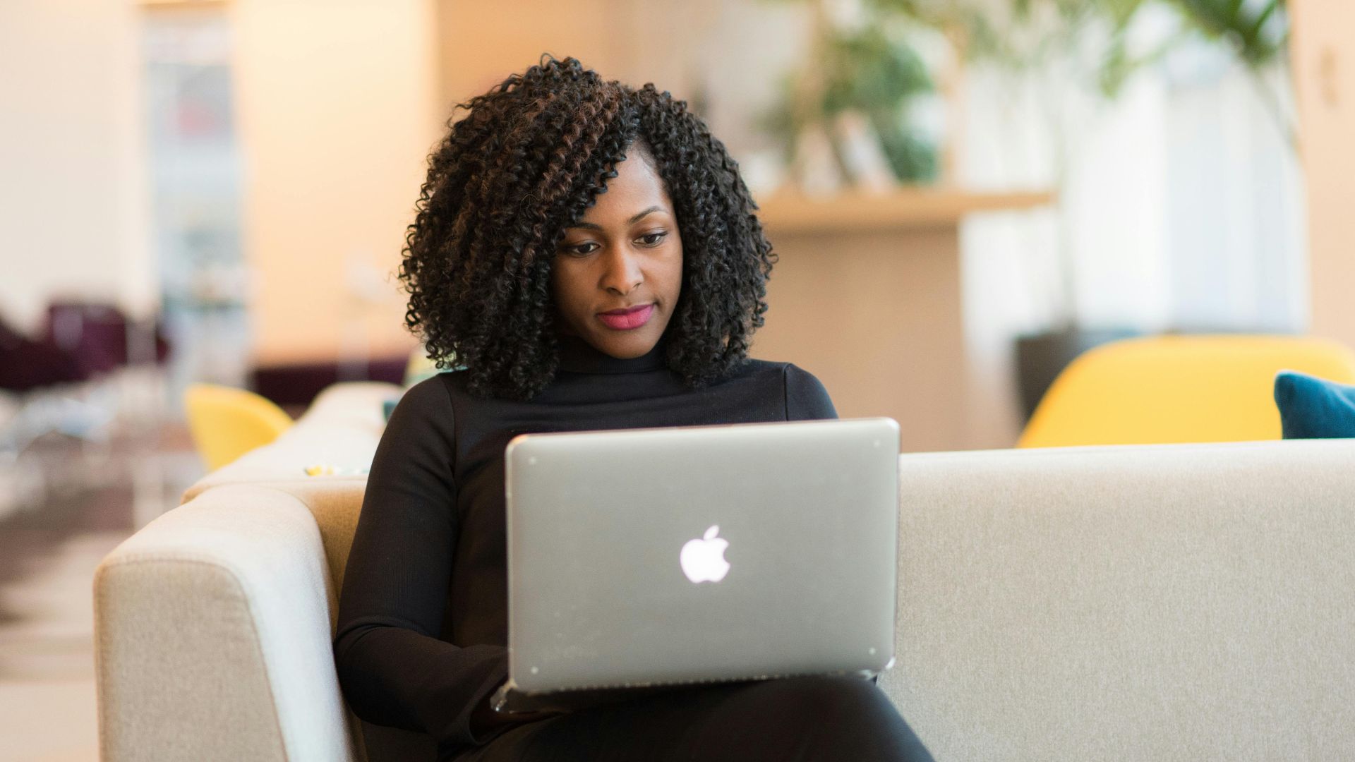 An African American woman working remotely on a laptop in a modern indoor setting.