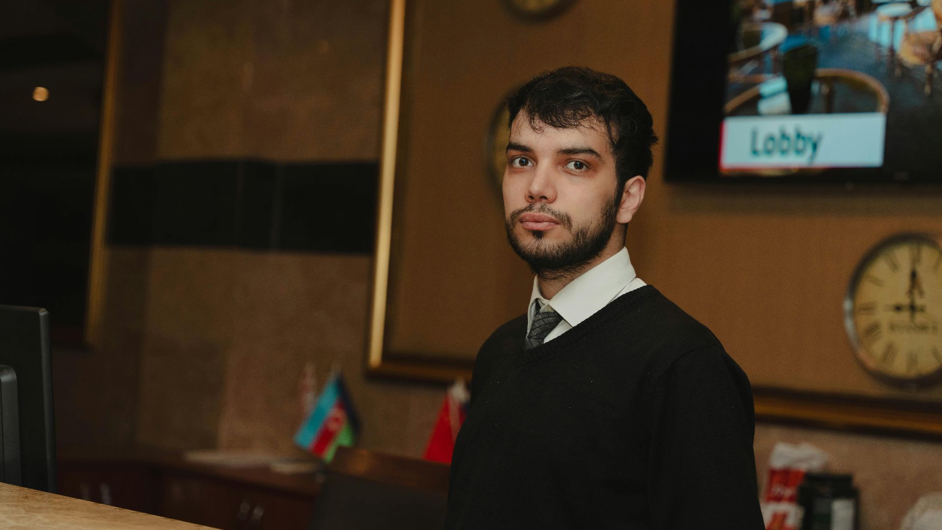 A hotel receptionist standing at the front desk in a hotel lobby, ready to assist guests.