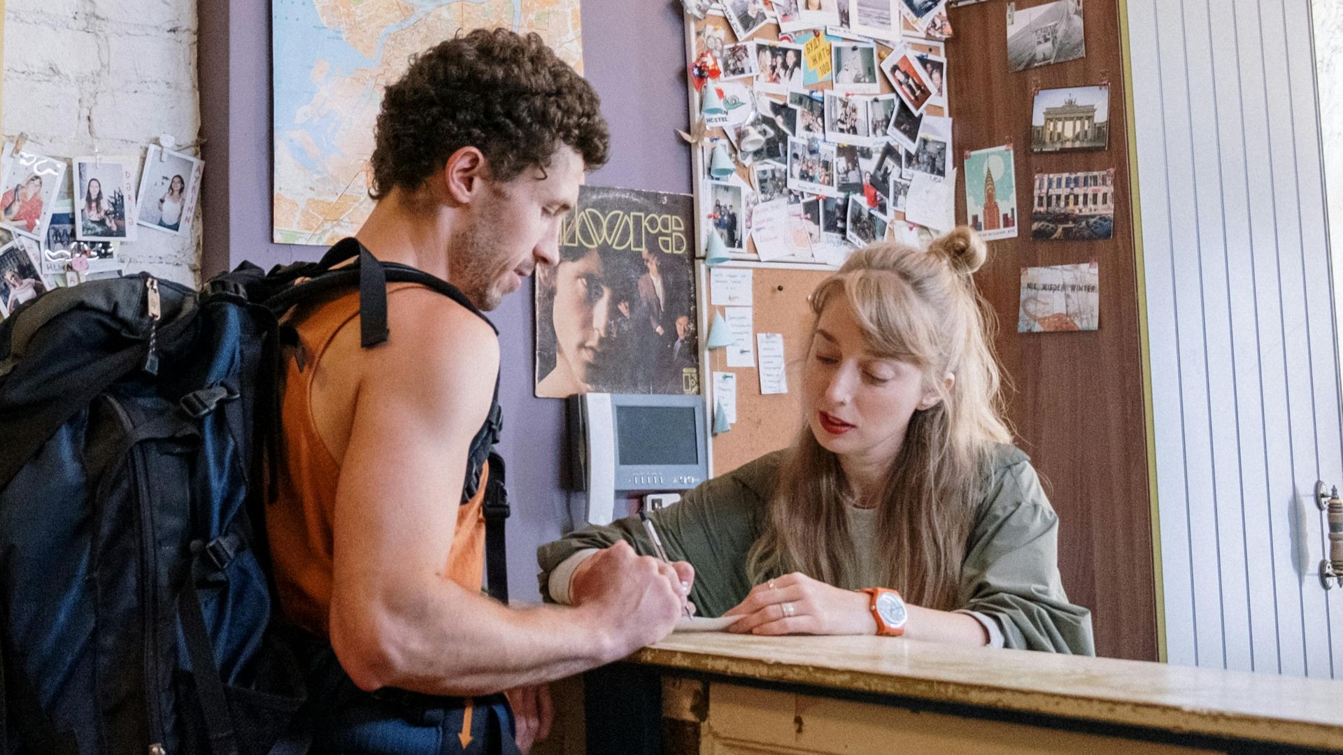 A backpacker at a hostel front desk getting assistance from a receptionist.