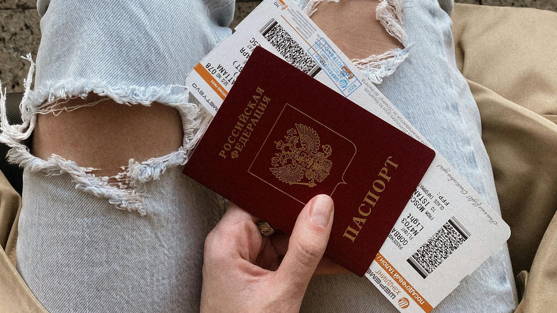 High-angle view of a person holding a passport and boarding passes, wearing ripped jeans and sneakers.