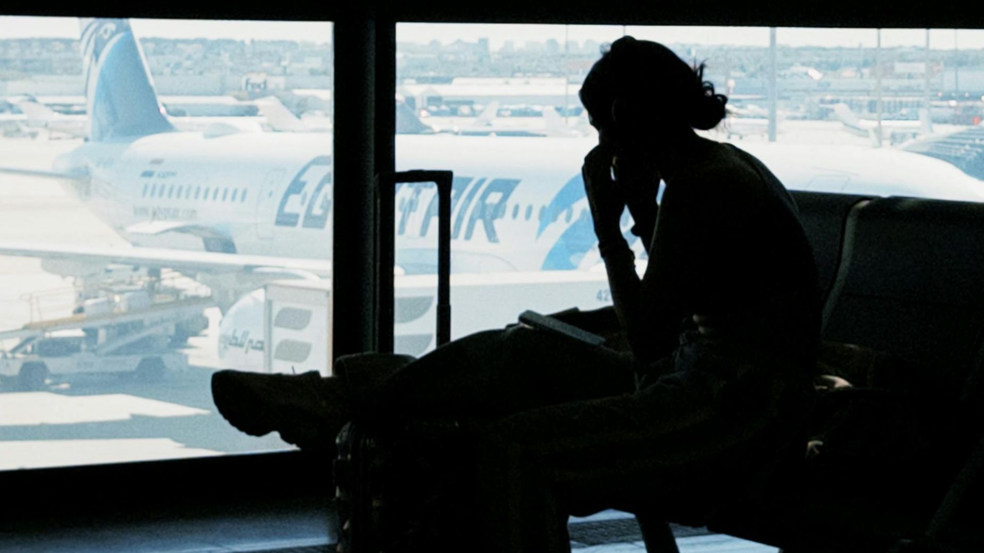 Silhouette of a person at an airport window with airplane view, embodying travel anticipation and solitude.