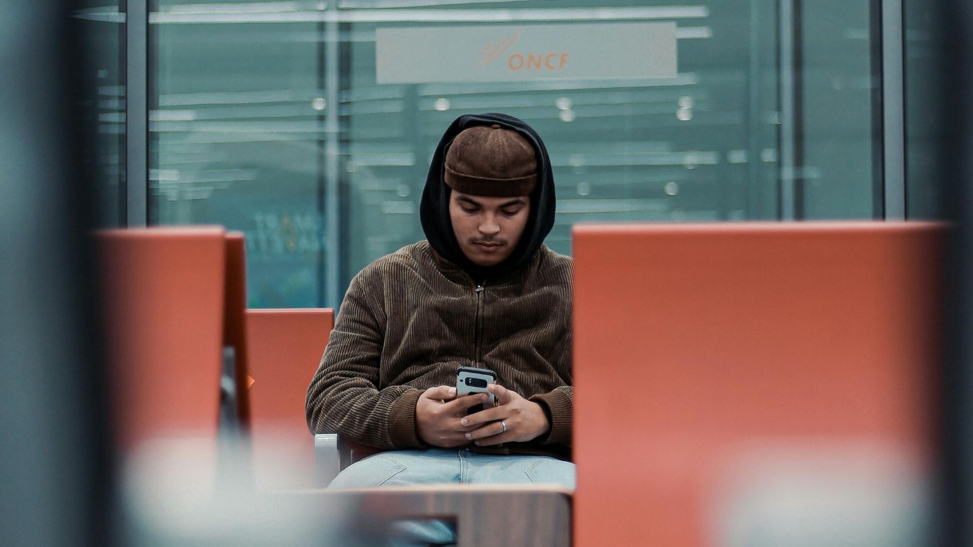 Young man sitting in an airport lounge in Rabat, Morocco, using a smartphone. Modern and relaxed setting.