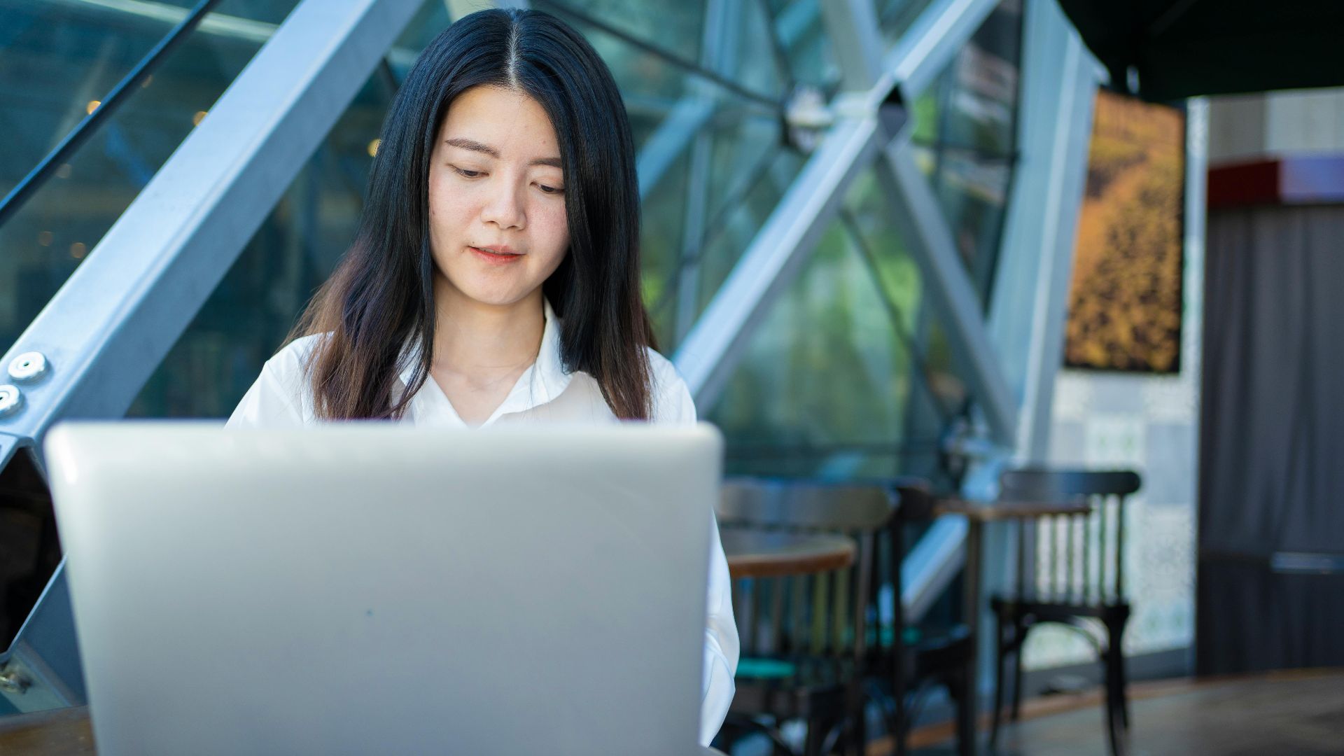 Asian woman working on a laptop in a modern cafe, exemplifying digital entrepreneurship and remote work.