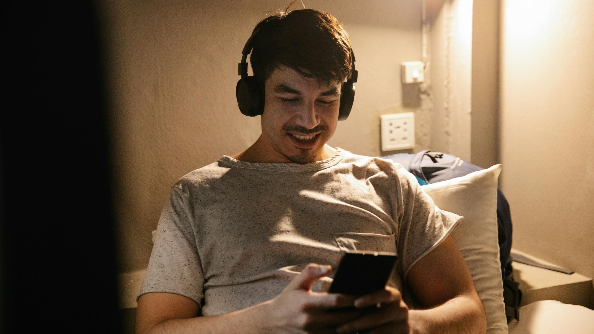 Young man enjoying music on headphones while relaxing in bed.