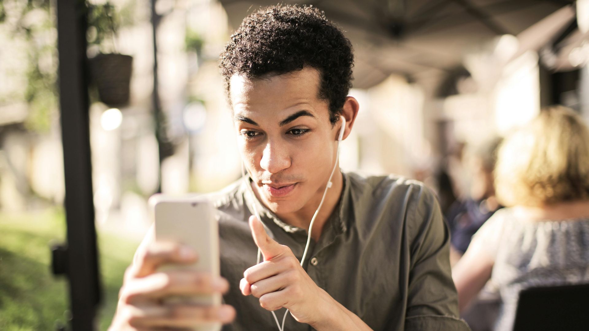 Young man wearing headphones, engaging in a video call outdoors on a sunny day.