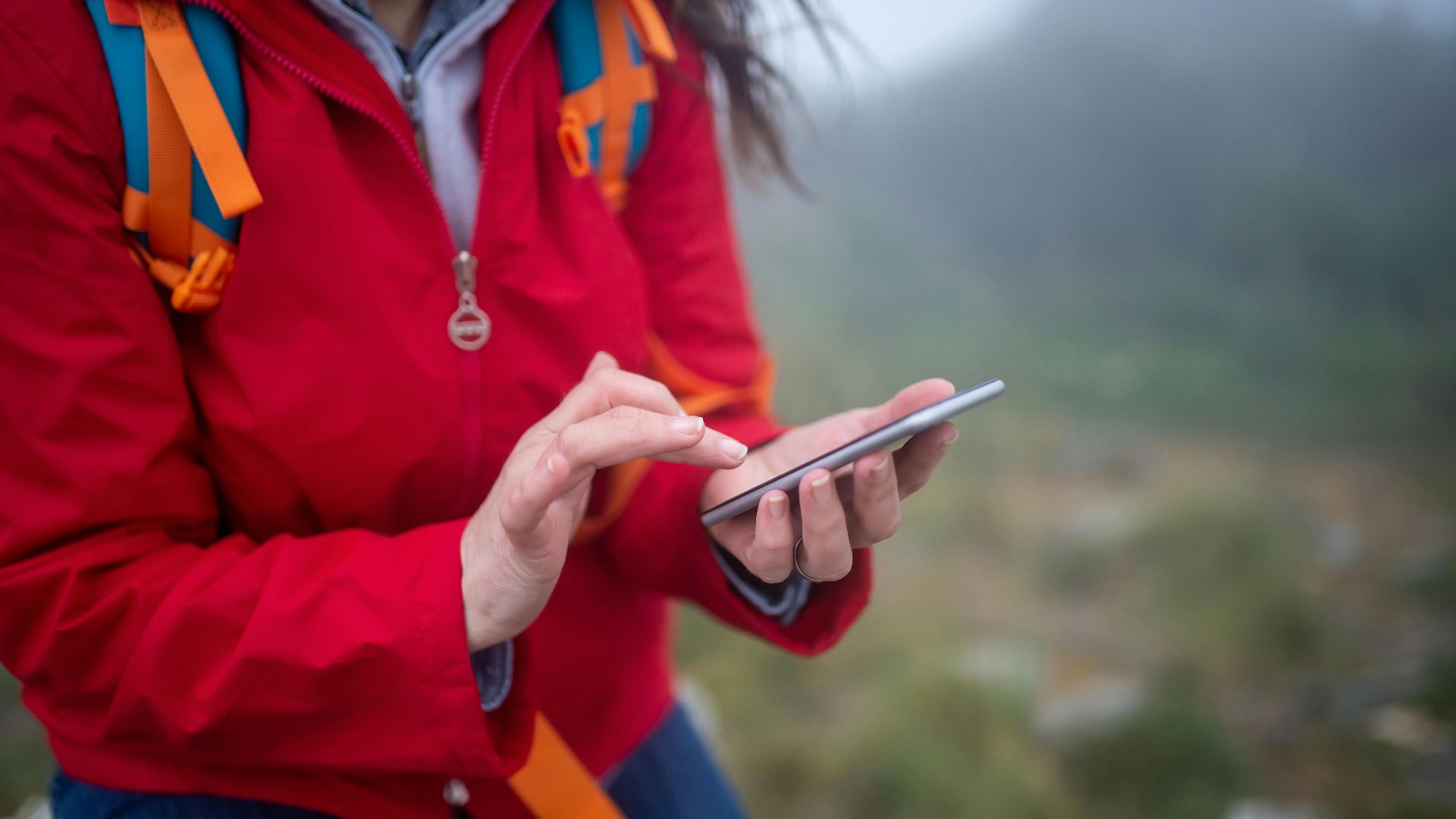 Close-up of a hiker in Portugal using a smartphone outdoors on a foggy day.