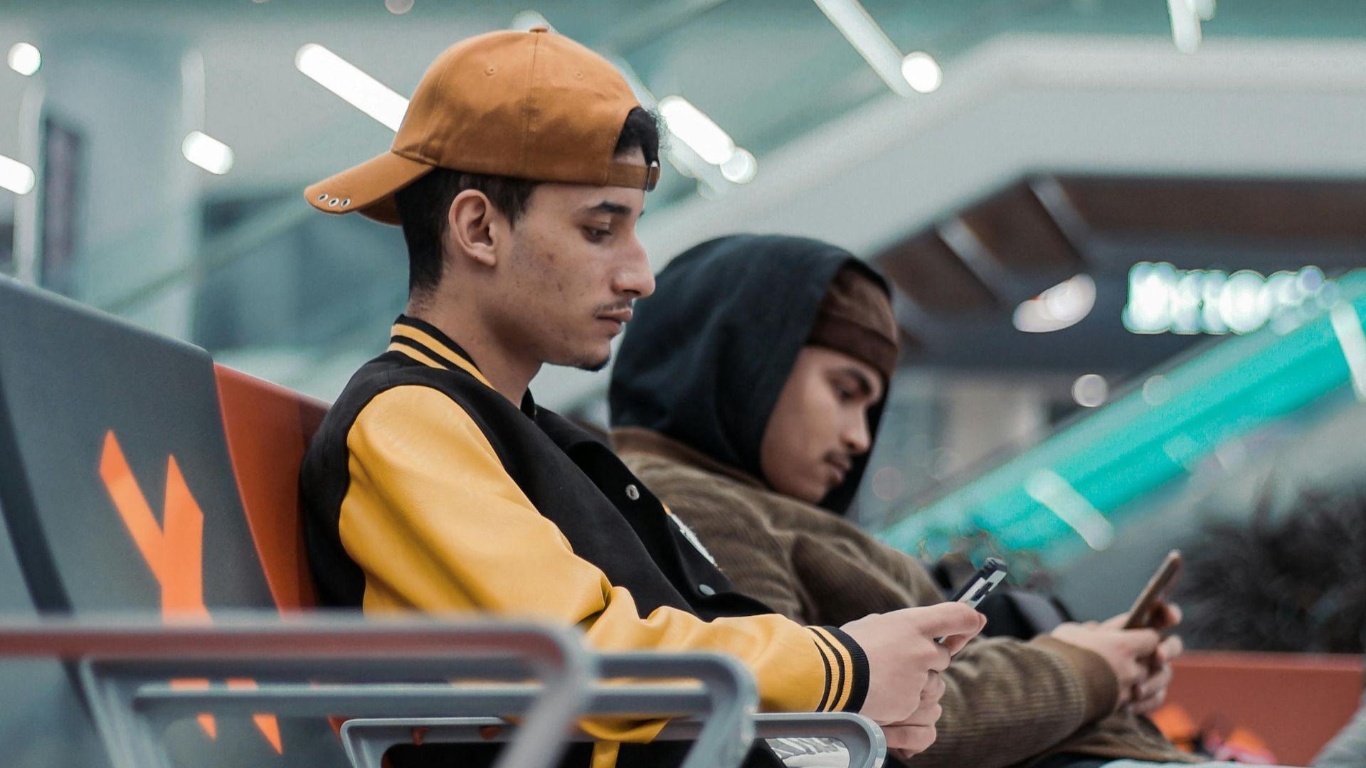Two young men using smartphones while seated at Rabat Airport terminal, illustrating travel connectivity.