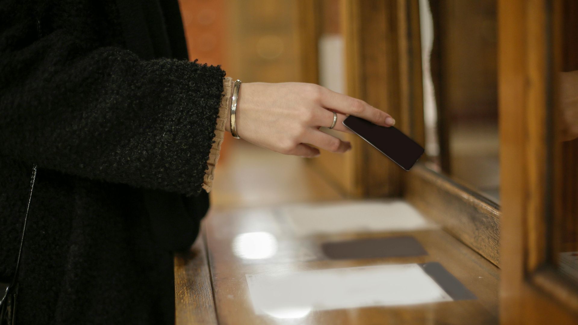 Close-up of a woman's hand using a black card for payment at an indoor counter.