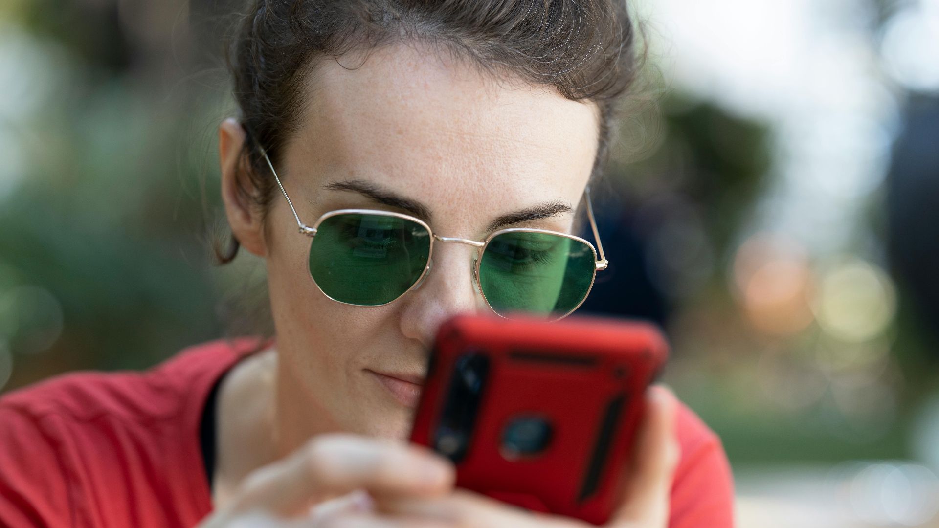 A woman in sunglasses attentively using a smartphone outdoors. Focus on technology and leisure.
