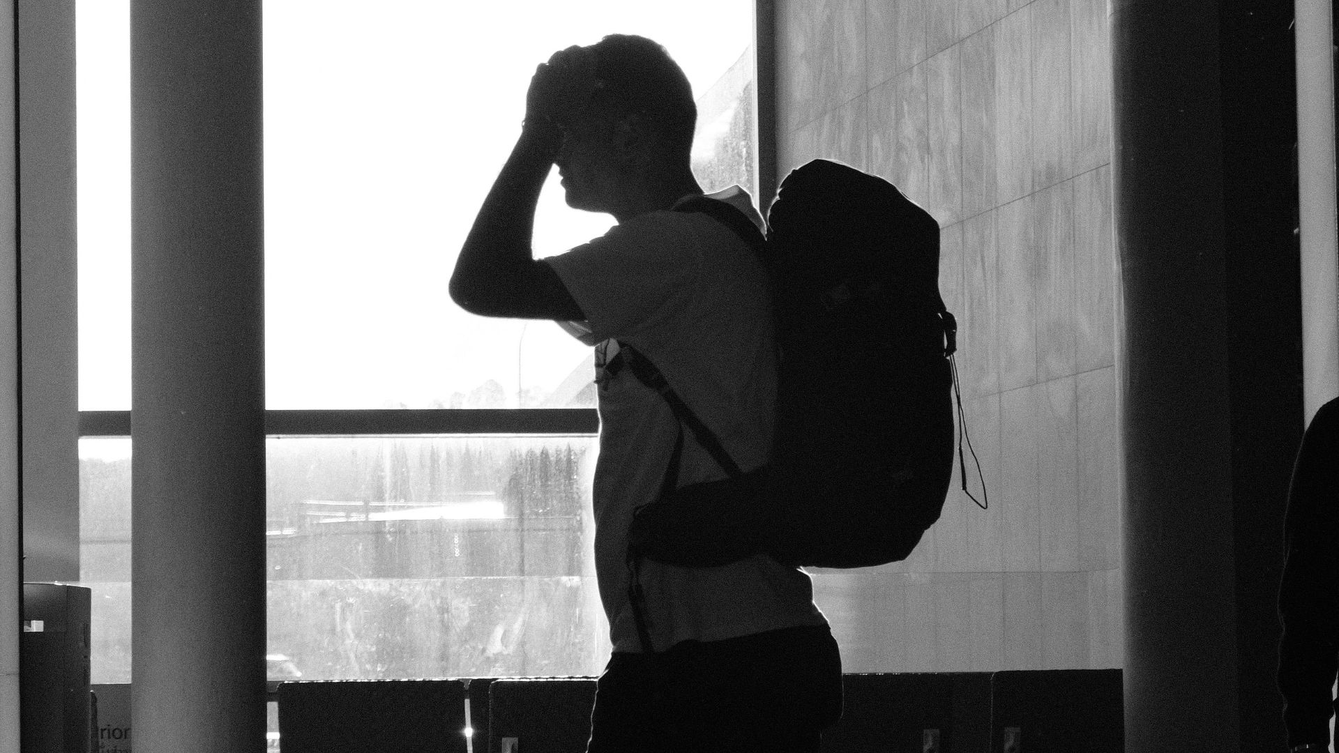 Silhouette of a man walking with a backpack at an airport terminal.